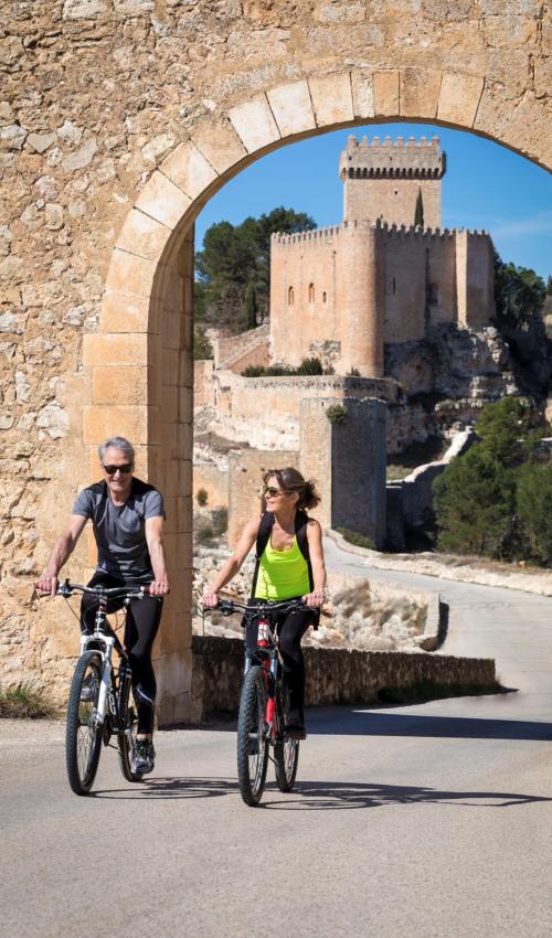 Una pareja de turistas circula en bicicleta con el castillo de Alarcón de fondo